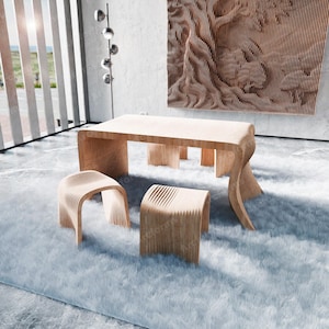 Puede incluir: Una mesa de madera clara y cuatro taburetes a juego con un diseño ondulado. La mesa y los taburetes están sobre una alfombra blanca mullida en una habitación moderna con una gran ventana y una escultura de pared de madera.