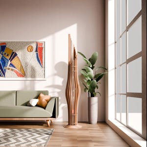 May include: A modern living room with a light green sofa, a wooden floor, and a large window. A tall, wooden floor lamp with a geometric design stands in the corner of the room. A potted plant with green leaves sits on the floor next to the lamp.