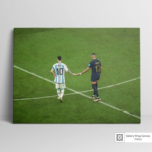 May include: Two soccer players, one in a blue and white jersey with the number 10 and the name "MESSI" on the back, and the other in a dark blue jersey with the number 10 and the name "MBAPPE" on the back, shake hands on a green soccer field.