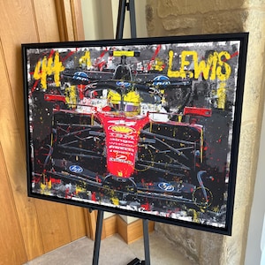 Puede incluir: Obra de arte enmarcada de un coche de carreras de Fórmula 1, con el número "44" y el nombre "LEWIS" en amarillo. El coche es principalmente rojo y negro, con logotipos de patrocinadores. La obra tiene un estilo abstracto con salpicaduras de color.
