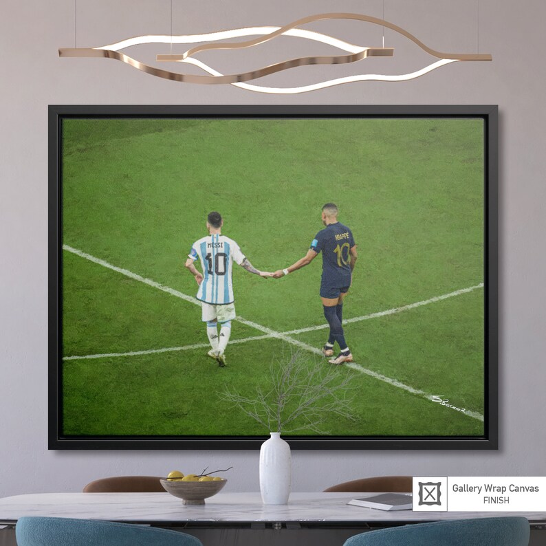 May include: A black framed canvas print of two soccer players, Lionel Messi and Kylian Mbapp&eacute;, shaking hands on a green soccer field. Messi is wearing a light blue and white jersey with the number 10 and Mbapp&eacute; is wearing a dark blue jersey with the number 10. The image is a close-up of the players from the waist up.
