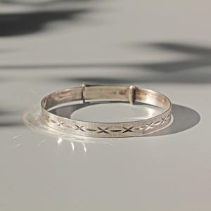 May include: A silver expandable bangle bracelet with a delicate criss-cross pattern.