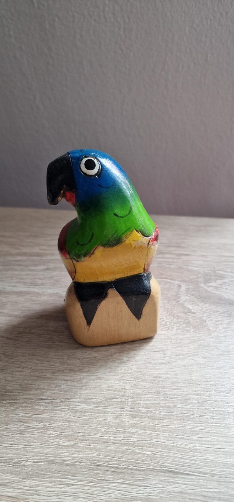 May include: Hand-painted wooden parrot figurine with blue, green, yellow, and black colors. The parrot is perched on a wooden base.