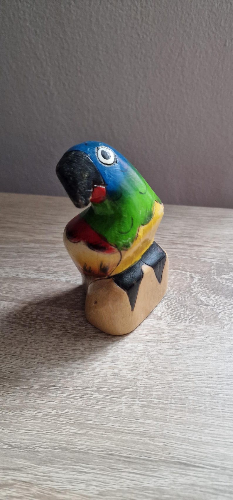 May include: Hand-painted wooden parrot figurine with blue, green, yellow, red, and black colors. The parrot is perched on a wooden base.
