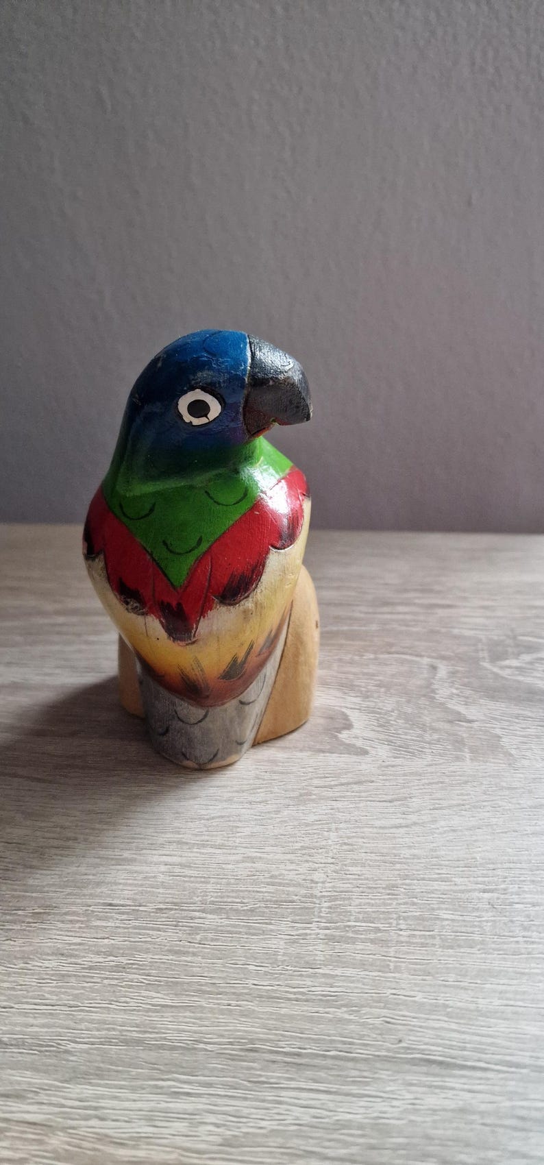 May include: A wooden parrot figurine painted in blue, green, red, and yellow. The parrot has a black beak and a white eye.