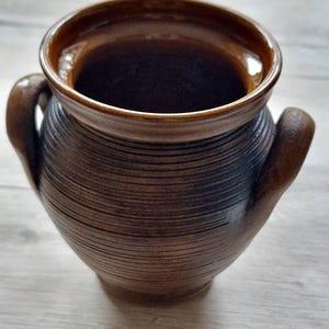Op de afbeelding: Een bruine keramische vaas met twee handvatten. De vaas heeft een getextureerd, gestreept ontwerp.