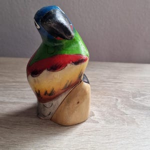 May include: Hand-painted wooden parrot figurine with blue, green, red, and yellow colors. The parrot is perched on a wooden base.