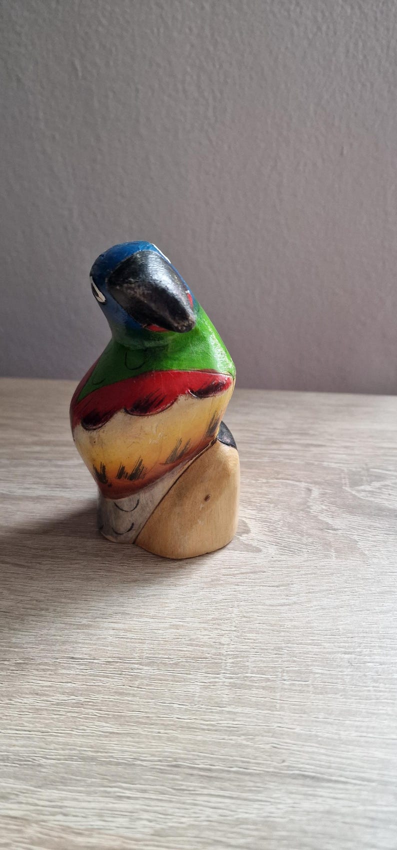 May include: Hand-painted wooden parrot figurine with blue, green, red, and yellow colors. The parrot is perched on a wooden base.