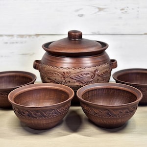 Puede incluir: Un juego de utensilios de cocina de arcilla marrón que consta de una olla con tapa y dos asas laterales, junto con cuatro cuencos a juego. Cada pieza presenta un patrón de hojas en relieve en el exterior, con un acabado uniforme de color marrón oscuro.