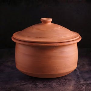 Puede incluir: Una olla de barro de color terracota con su tapa a juego. La olla presenta un acabado mate y liso, con un cuerpo cilíndrico ancho y una base ligeramente redondeada. La tapa tiene un pequeño pomo central y un diseño de borde circular simple.