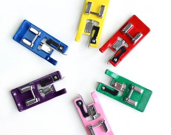 May include: Six different colored sewing machine presser feet. The feet are made of metal and have a silver finish. The colors are blue, yellow, red, green, purple, and pink.