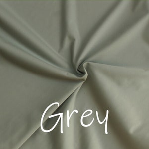May include: A close-up of a smooth, grey fabric with a slight sheen. The fabric is folded and draped, creating soft folds and curves. The word "Grey" is written in white text on the fabric.