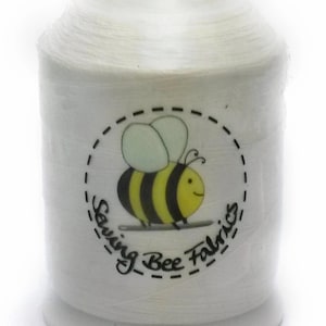 May include: White spool of thread with a cartoon bee logo. The bee is yellow and black with a smiling face and light green wings. The text "Sewing Bee Fabrics" is around the bee.