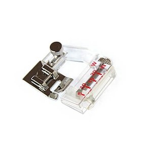 May include: A clear plastic sewing machine foot with a metal adjustment knob and a ruler marked in millimetres. The ruler is labelled "5 10 15 20 W".