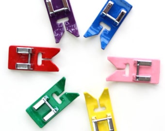 May include: Six colorful sewing machine presser feet with metal bars. The feet are in a starburst pattern and are red, green, yellow, pink, blue, and purple.