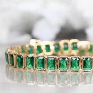 May include: A gold bracelet with emerald green rectangular stones.