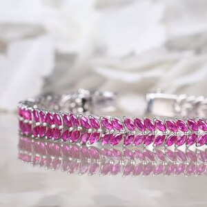 Puede incluir: Un brazalete de plata con una doble fila de piedras preciosas rosas en forma de marquesa. El brazalete se refleja en una superficie blanca.