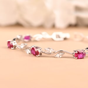 May include: A silver-toned bracelet featuring a series of oval-cut vibrant pink stones alternating with marquise-cut clear white stones. The metal links are shaped into delicate, flowing vine-like curves connecting each gemstone setting.