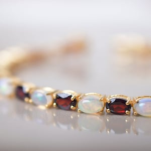 May include: A gold bracelet with alternating white opal and red garnet stones.