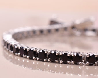 May include: A silver tennis bracelet with black round gemstones.