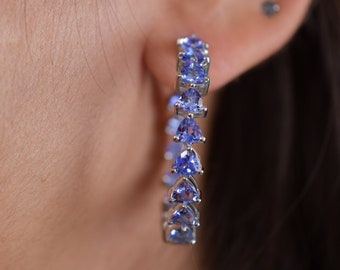 May include: A pair of silver hoop earrings with a row of blue triangular gemstones.