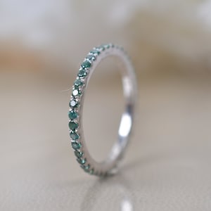 Puede incluir: Una fina banda de plata con una fila de pequeñas piedras preciosas verdes engastadas alrededor de todo el anillo.
