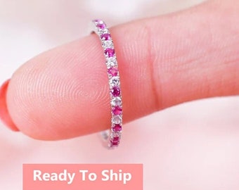 May include: A delicate eternity band ring with alternating pink and white gemstones. The ring is set in a silver metal band.
