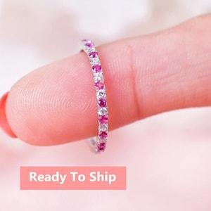 以下が含まれることがあります： 交互にピンクと白の宝石が並んだ、繊細なエタニティバンドリング。リングはシルバーメタルのバンドにセットされています。