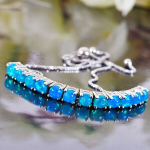 Op de afbeelding: Een zilveren kettingarmband met een rij ovale blauwe opaal edelstenen.
