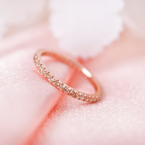 May include: A delicate rose gold band ring with a row of small sparkling diamonds.
