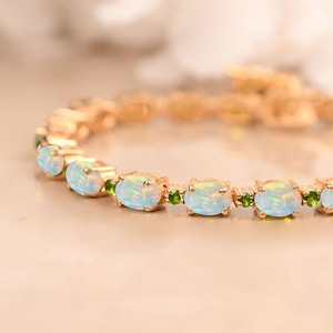 May include: A gold bracelet with oval opals and small green gemstones. The opals have a milky, iridescent appearance, and the bracelet is set on a gold chain. The gemstones are evenly spaced along the bracelet.