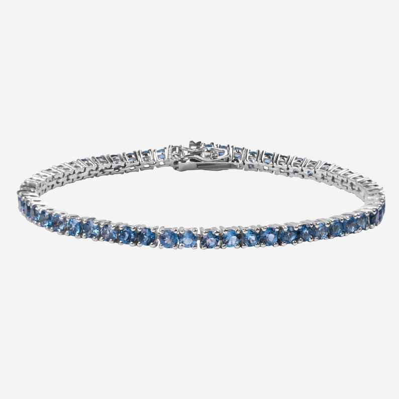 May include: A silver tennis bracelet with blue gemstones.