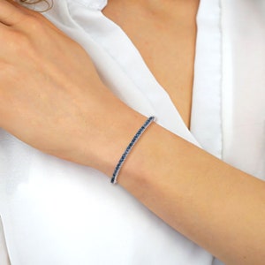 May include: A silver bracelet with a row of blue sapphires.