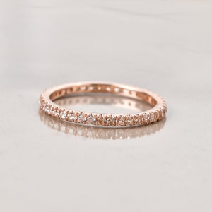 May include: A rose gold eternity band with a row of small, clear gemstones.