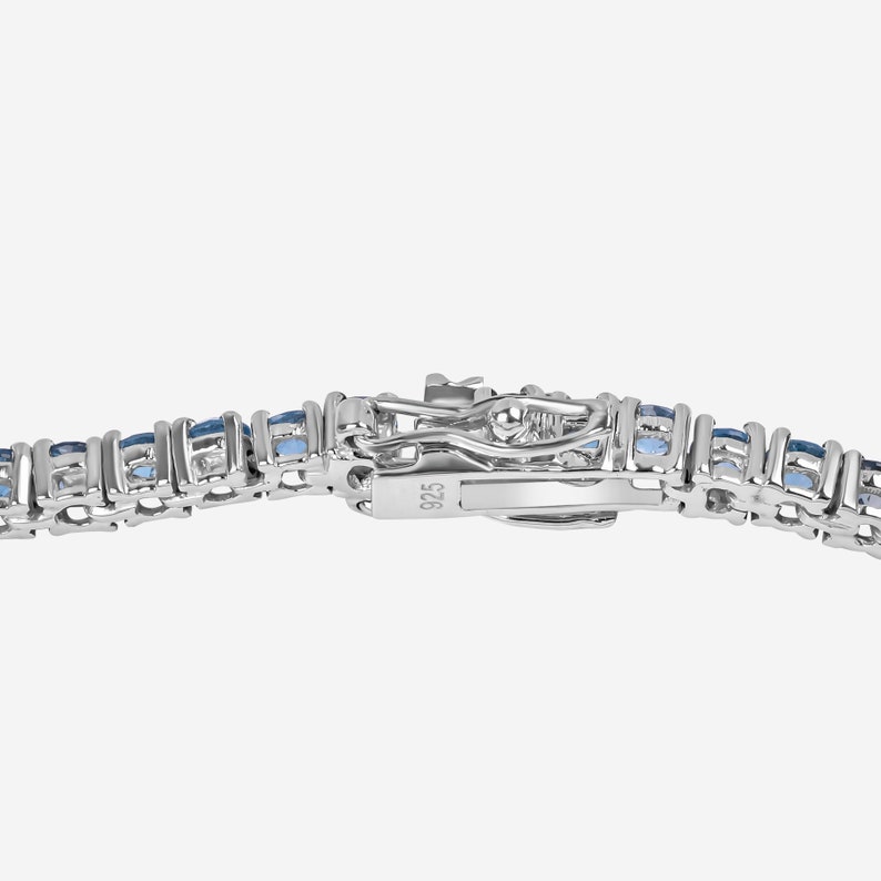 May include: A silver tennis bracelet with a row of blue gemstones. The clasp is marked with the number 925.