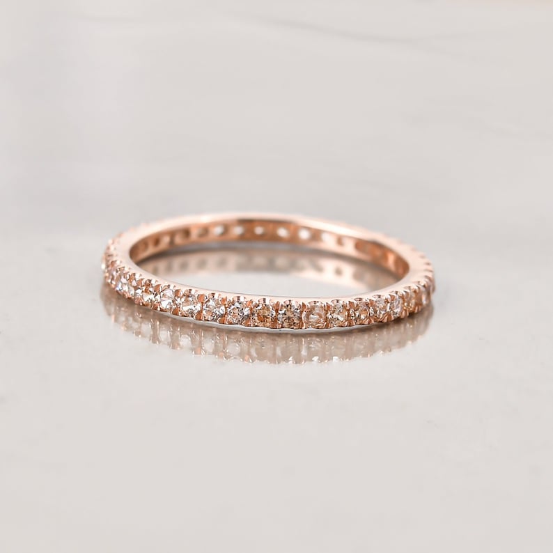 May include: A rose gold band ring with a row of small clear stones around the entire band.