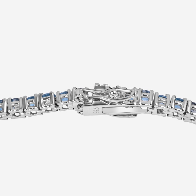 May include: A silver tennis bracelet with a row of blue gemstones. The clasp is marked with the number 925.