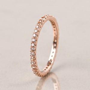 May include: A rose gold band ring with a row of small diamonds encircling the band.