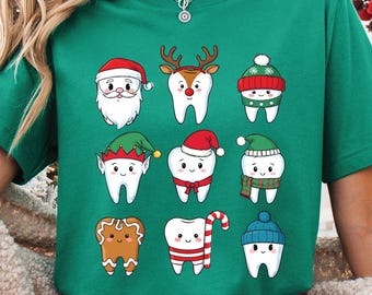 May include: Green short-sleeve t-shirt featuring cartoon teeth dressed as Christmas characters, including Santa, reindeer, and elves. The design includes a gingerbread tooth and a tooth with a candy cane. The shirt is paired with red and white plaid pajama pants.