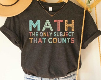 May include: Dark grey heather V-neck t-shirt with the text "MATH THE ONLY SUBJECT THAT COUNTS" in colorful letters. The shirt is being modeled on a person wearing blue jeans and a brown woven bag.