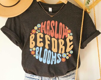 May include: Dark grey heather t-shirt with a graphic of colorful flowers and the text "Maslow Before Blooms".