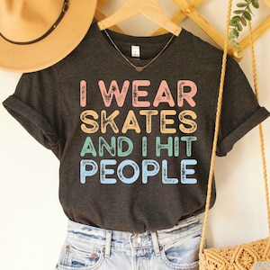 May include: Dark grey heather V-neck t-shirt with the text "I wear skates and I hit people" in rainbow colours.