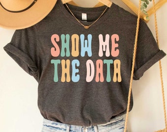 May include: A dark grey heather t-shirt with the text "Show Me The Data" in colorful retro font.