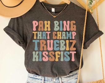 May include: Dark grey heather t-shirt with the text "Pah Bing That Champ Truebiz Kissfist" in colorful retro font.