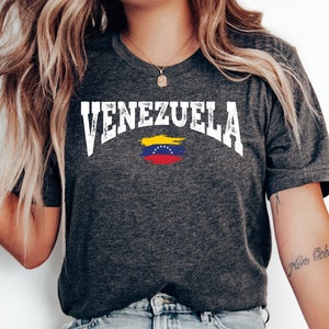 May include: Dark grey heather t-shirt with a white distressed graphic of the word "VENEZUELA" and the Venezuelan flag.