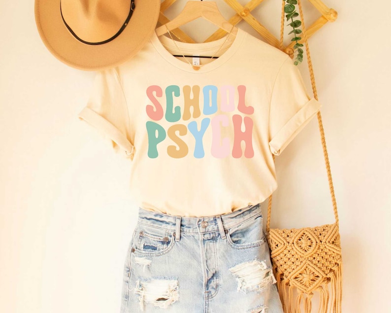 May include: A light beige t-shirt with the text "SCHOOL PSYCH" in colorful retro font.