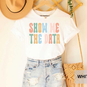 May include: White t-shirt with the text "SHOW ME THE DATA" in colorful retro font.