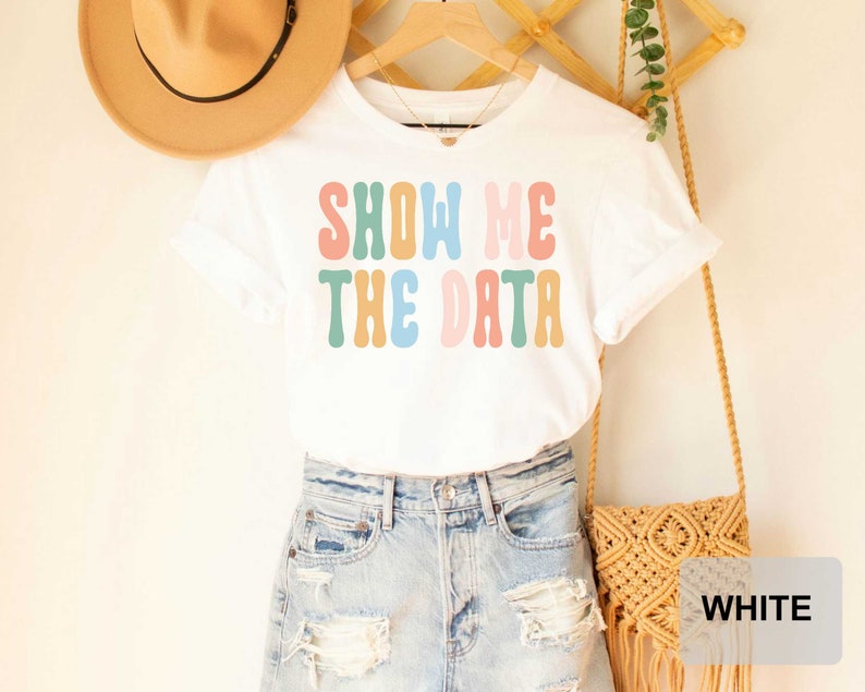 May include: White t-shirt with the text "SHOW ME THE DATA" in colorful retro font.