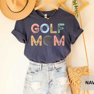 May include: Navy blue t-shirt with the text "GOLF MOM" in colorful letters with a golf ball graphic.