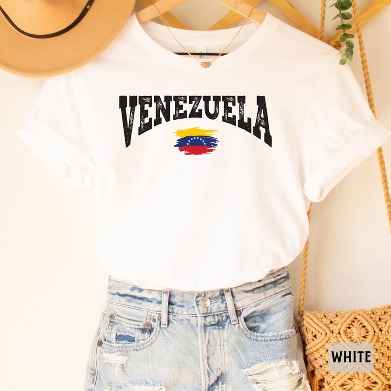 May include: White t-shirt with a black distressed graphic of the word "VENEZUELA" and a stylized Venezuelan flag.